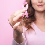 Woman in pink sweater with pink ribbon supporting breast cancer awareness campaign